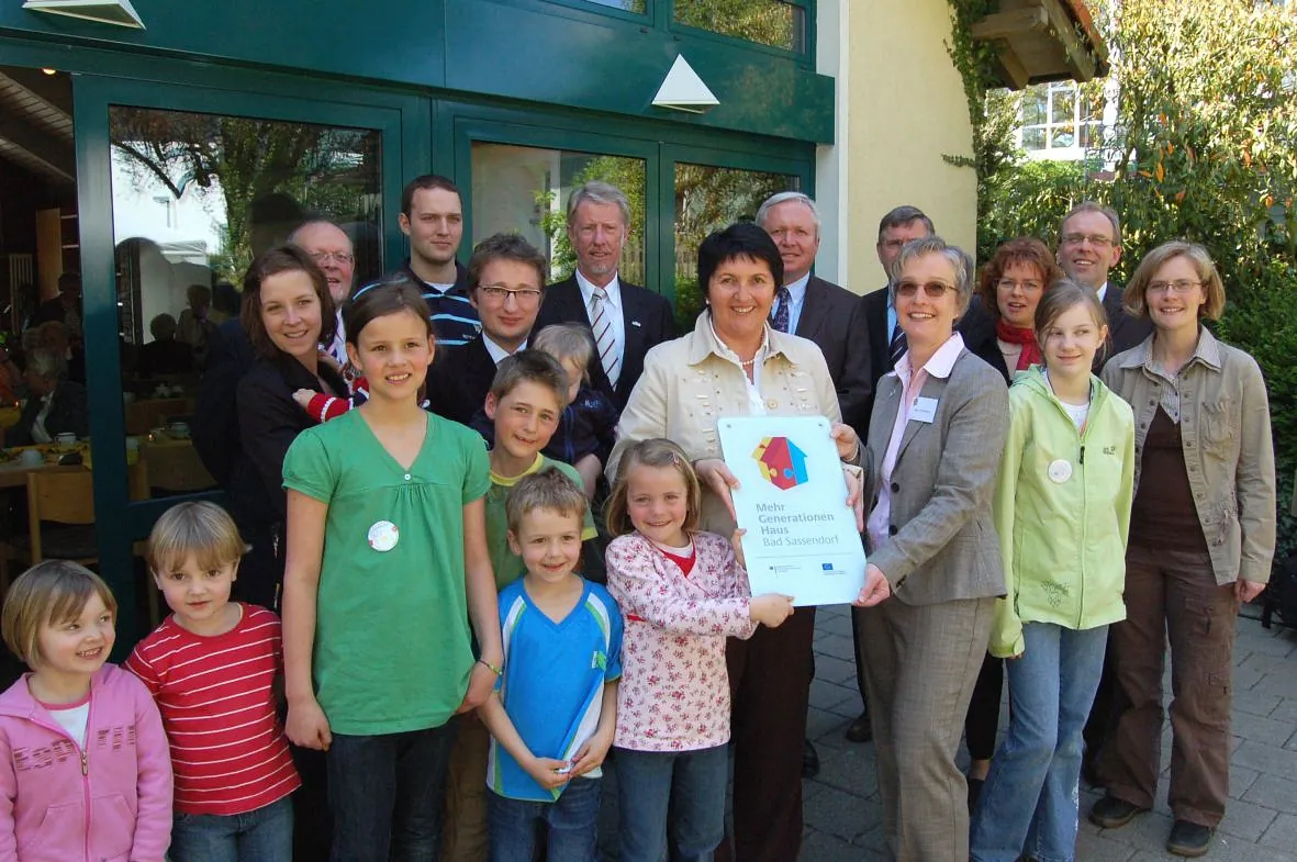 Foto mit einem Teil der eingeladenen Gesellschaft mit Frau Irgang, die das Eingangsschild des Hauses Präsentiert